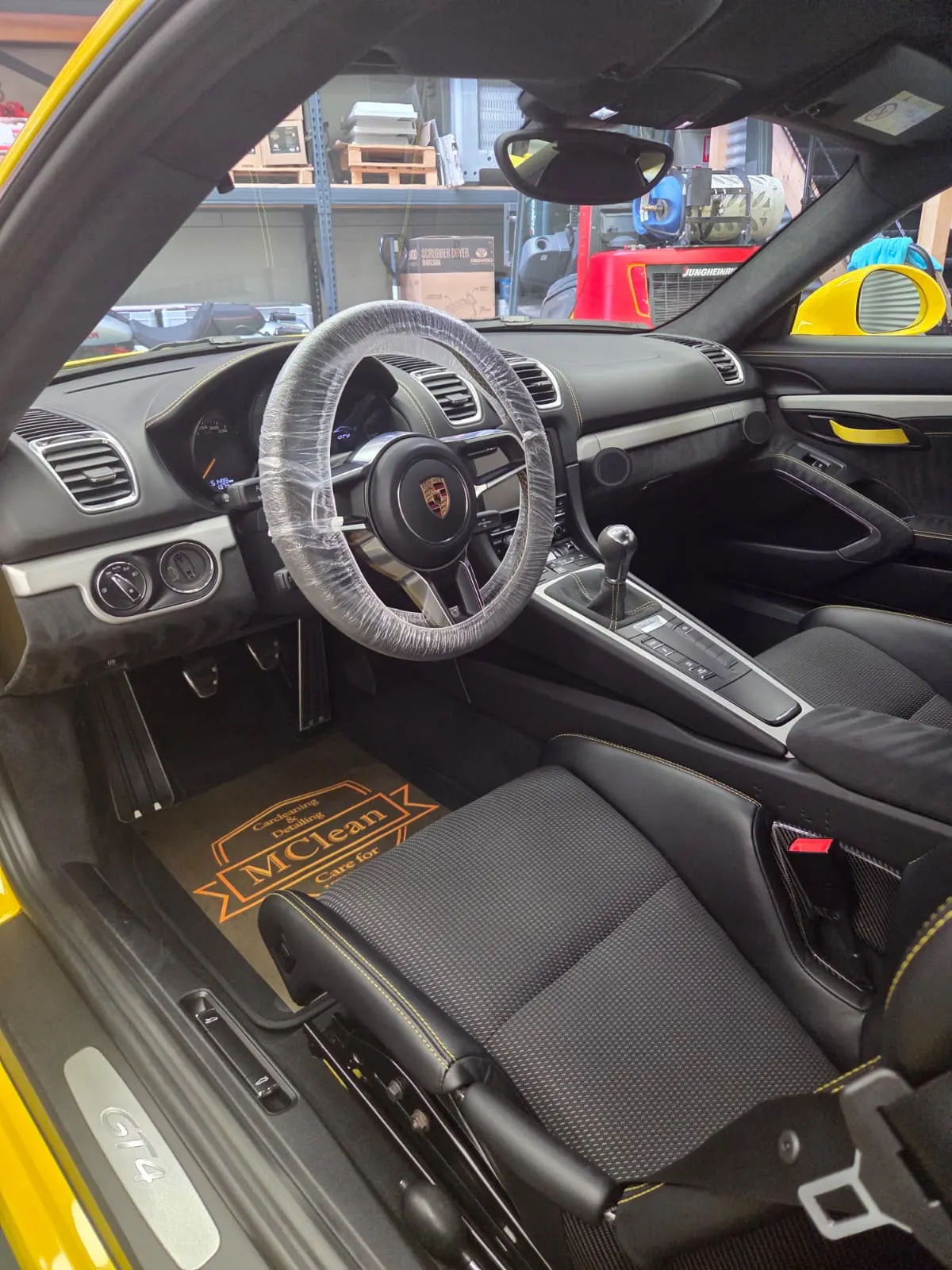 Interieur van een Porsche Cayman GT4, met een beschermhoes om het stuur en een mat van MClean