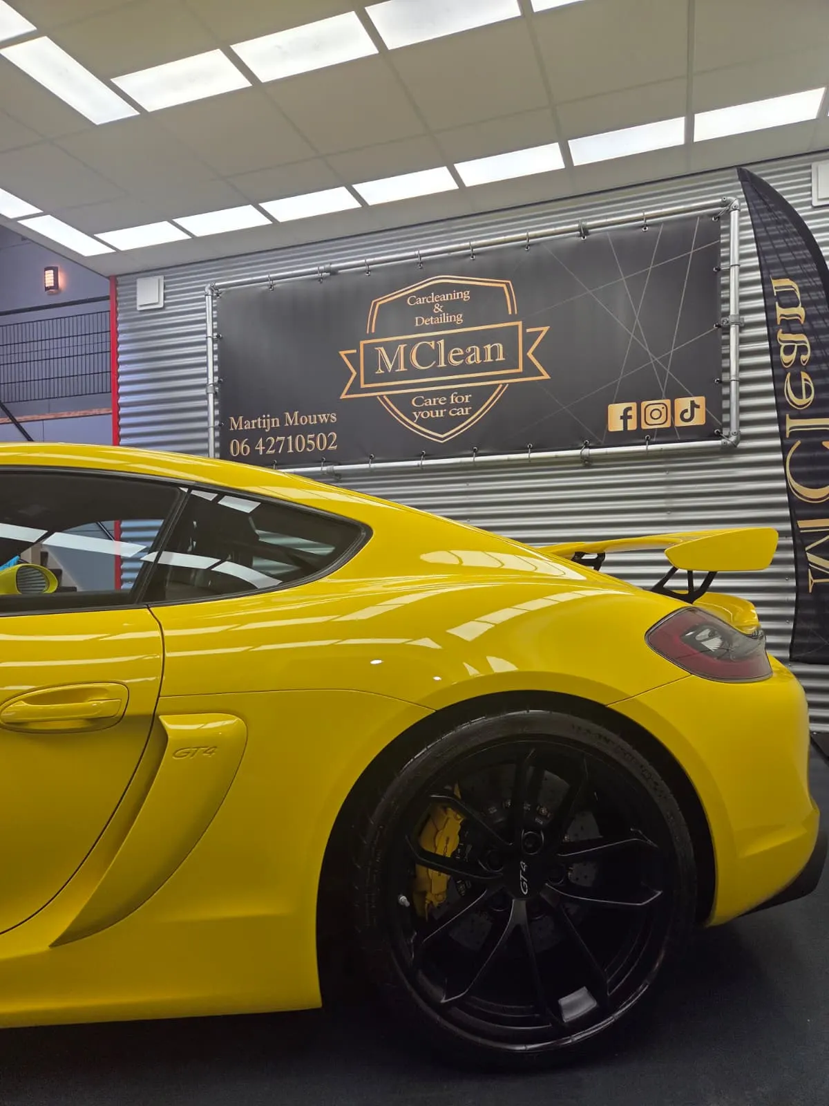 Gele Porsche Cayman GT4 voor de studiowand met het logo van MClean